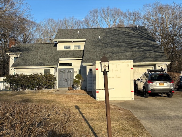 view of front facade featuring a chimney, driveway, an attached garage, and roof with shingles