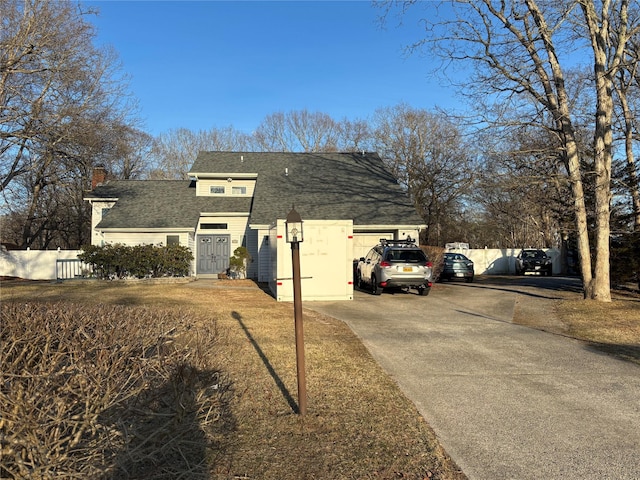 view of front of property with a chimney, a shingled roof, driveway, and fence