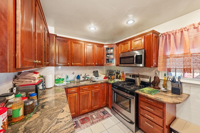 kitchen featuring light stone counters, a sink, glass insert cabinets, appliances with stainless steel finishes, and tasteful backsplash