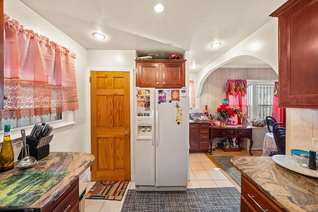 kitchen with stone counters, light tile patterned flooring, recessed lighting, arched walkways, and white fridge with ice dispenser