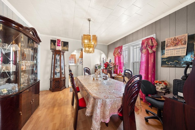 dining area with ornamental molding, arched walkways, and light wood-type flooring