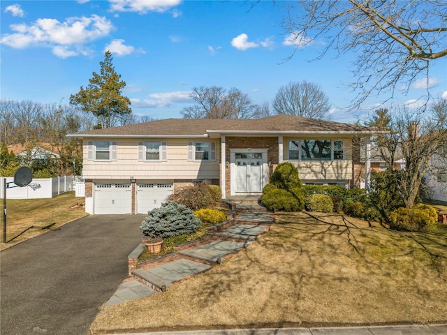 raised ranch with a front yard, fence, driveway, an attached garage, and brick siding