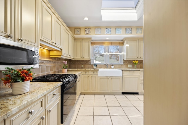 kitchen with black gas range oven, stainless steel microwave, light tile patterned floors, cream cabinetry, and a sink