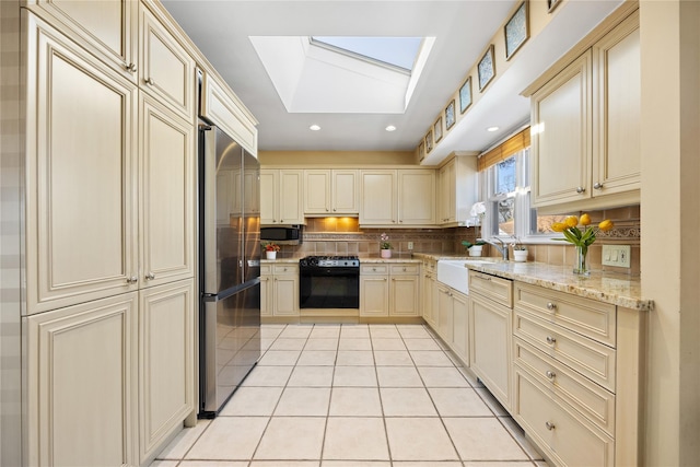 kitchen with cream cabinetry, appliances with stainless steel finishes, a skylight, and a sink