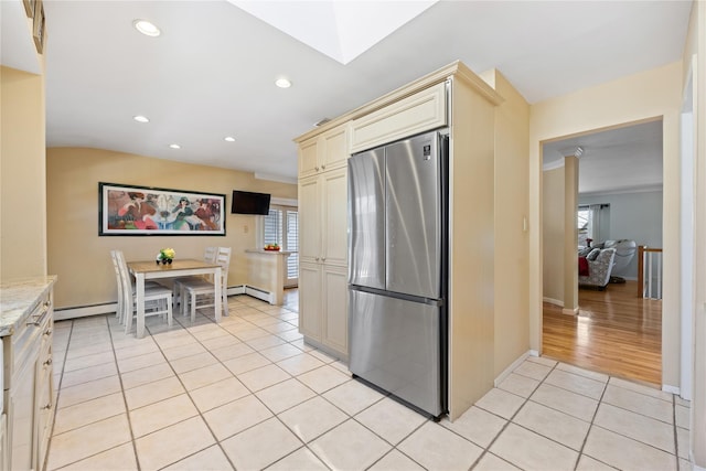 kitchen featuring light stone counters, a skylight, cream cabinets, freestanding refrigerator, and light tile patterned flooring