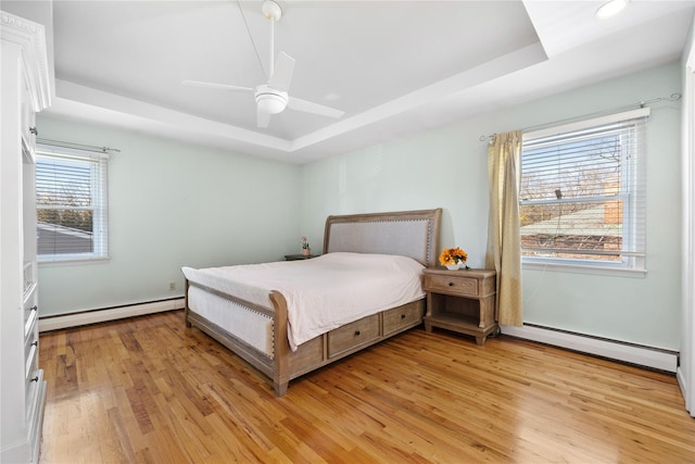 bedroom featuring light wood finished floors, ceiling fan, a tray ceiling, and a baseboard radiator