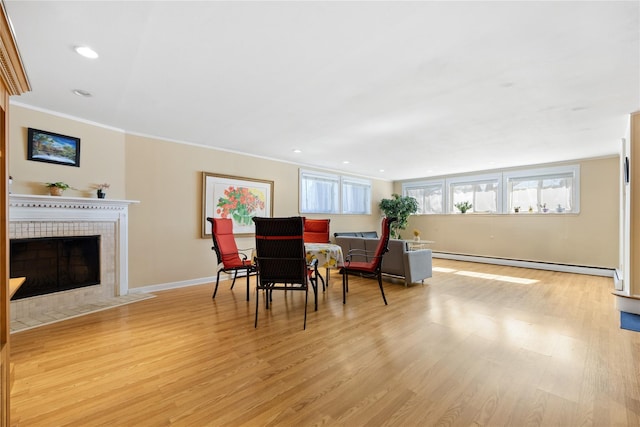 dining area featuring baseboards, a baseboard radiator, a tiled fireplace, crown molding, and light wood-type flooring