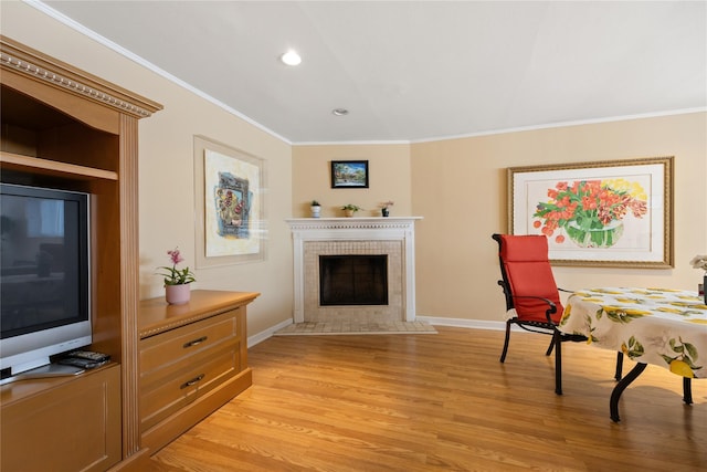 sitting room featuring baseboards, light wood finished floors, crown molding, and a tile fireplace