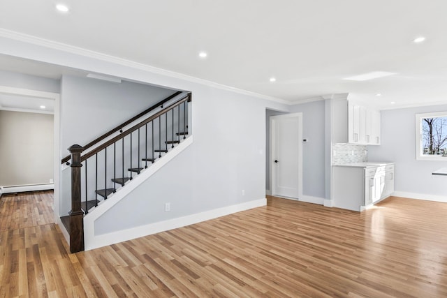 unfurnished living room with stairway, baseboards, light wood-style flooring, and crown molding