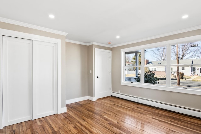 unfurnished bedroom with wood finished floors, crown molding, baseboards, and a baseboard radiator