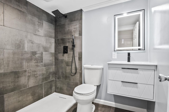 bathroom featuring toilet, a tile shower, crown molding, baseboards, and vanity