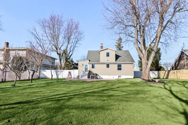 back of house with entry steps, a fenced backyard, a lawn, and a chimney