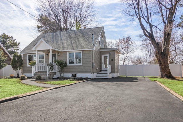 view of front facade with aphalt driveway, fence, a chimney, and a shingled roof