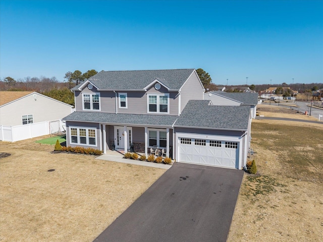 traditional-style home featuring fence, driveway, roof with shingles, a front lawn, and a garage