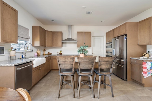 kitchen featuring visible vents, a sink, a kitchen island, stainless steel appliances, and wall chimney range hood