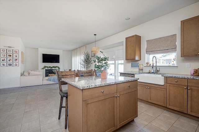 kitchen with a center island, a breakfast bar, light stone counters, brown cabinetry, and a sink