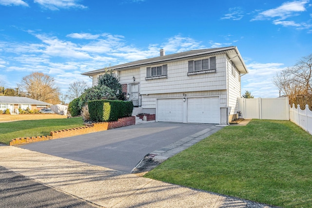 raised ranch with fence, an attached garage, a chimney, a front lawn, and aphalt driveway