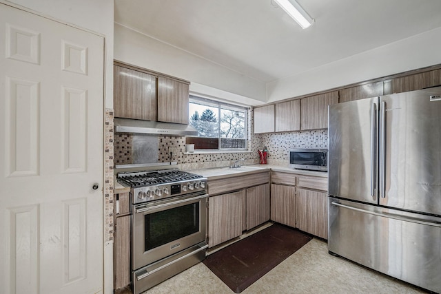 kitchen with a sink, light countertops, under cabinet range hood, appliances with stainless steel finishes, and tasteful backsplash