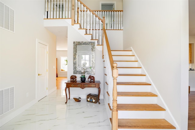 staircase with a towering ceiling, baseboards, visible vents, and marble finish floor