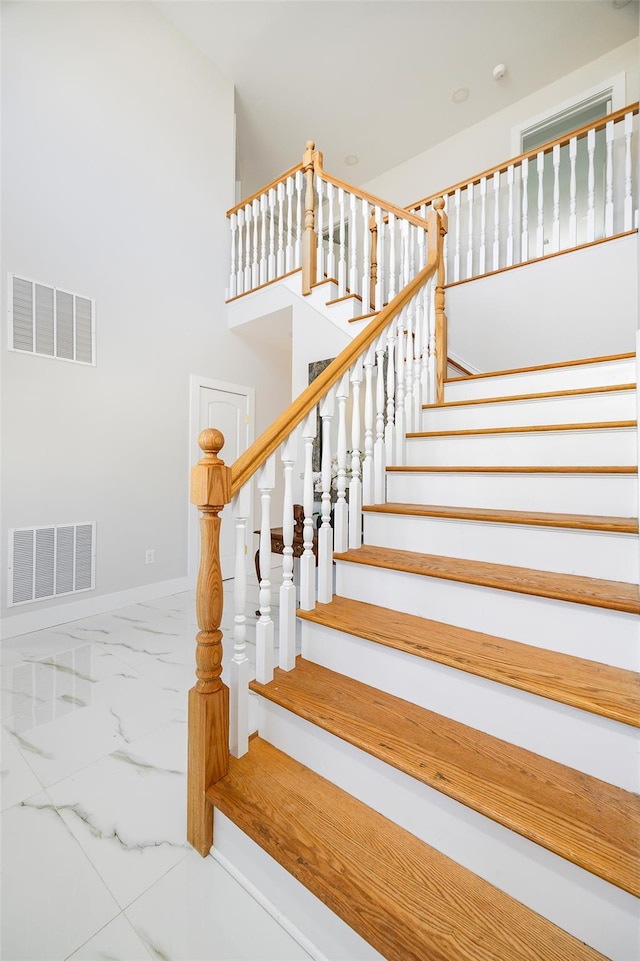 stairway with a high ceiling, baseboards, visible vents, and marble finish floor