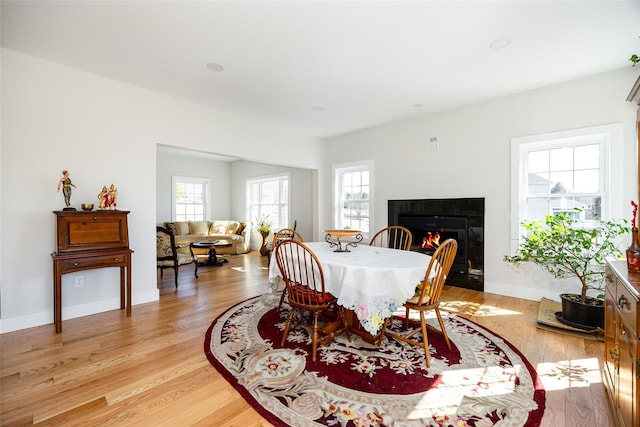 dining space with plenty of natural light, baseboards, light wood-type flooring, and a warm lit fireplace