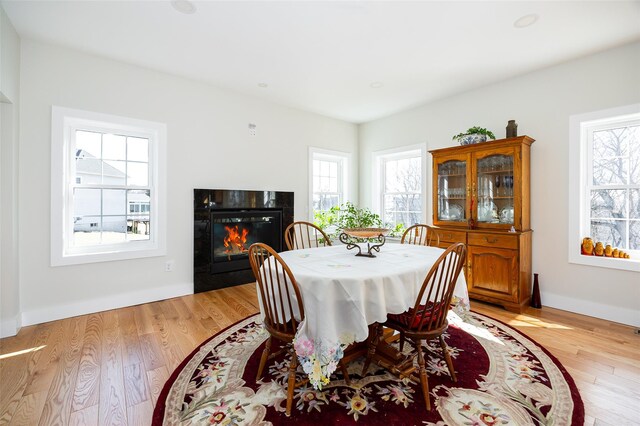 dining room with light wood-style flooring, a fireplace with flush hearth, and baseboards