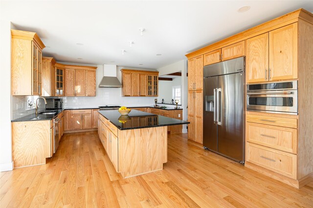 kitchen featuring light wood-style flooring, wall chimney exhaust hood, appliances with stainless steel finishes, and a kitchen island