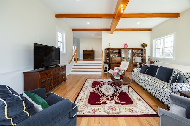 living area with beam ceiling, light wood-style flooring, and stairs