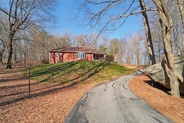 view of front facade featuring driveway, a chimney, and a front yard