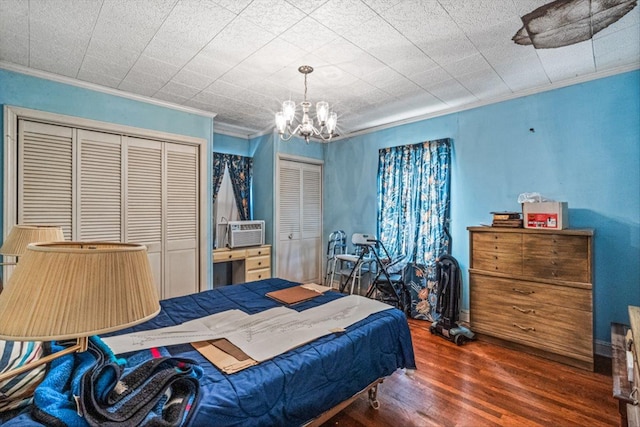 bedroom featuring two closets, ornamental molding, cooling unit, wood finished floors, and a notable chandelier