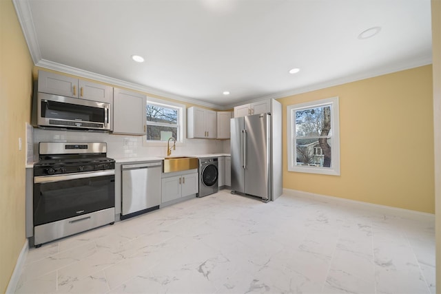 kitchen featuring crown molding, washer / dryer, marble finish floor, stainless steel appliances, and a sink