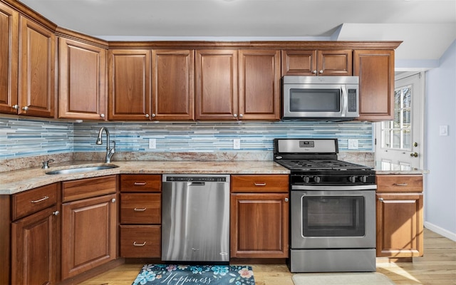 kitchen with light stone countertops, a sink, appliances with stainless steel finishes, tasteful backsplash, and brown cabinets