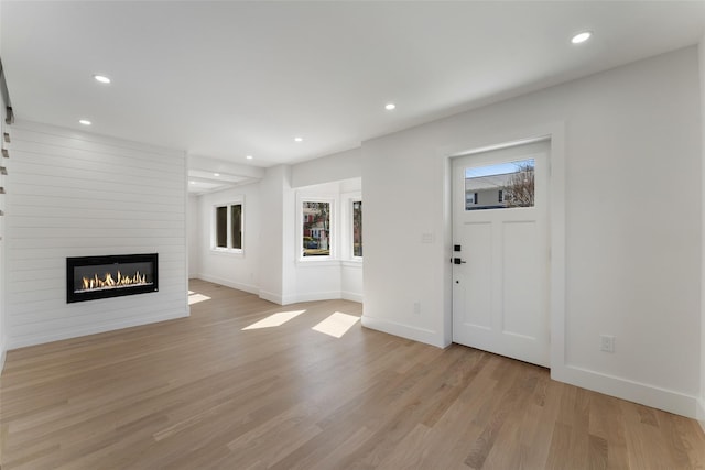 unfurnished living room featuring recessed lighting, light wood-type flooring, a large fireplace, and baseboards