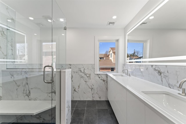 full bath featuring tile walls, visible vents, a marble finish shower, and a sink