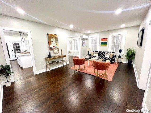 living area with dark wood finished floors, french doors, an AC wall unit, and baseboards