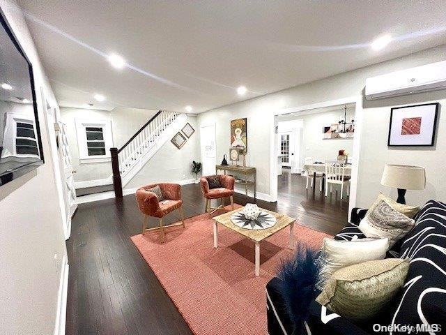 living area featuring stairs, baseboards, a wall mounted air conditioner, and hardwood / wood-style floors