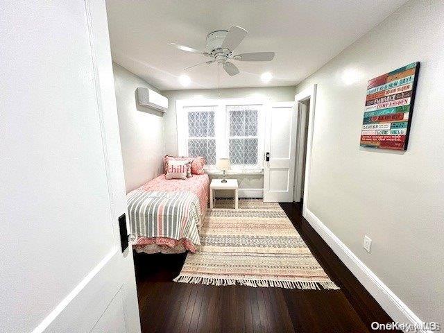 bedroom featuring an AC wall unit, baseboards, dark wood-type flooring, and ceiling fan