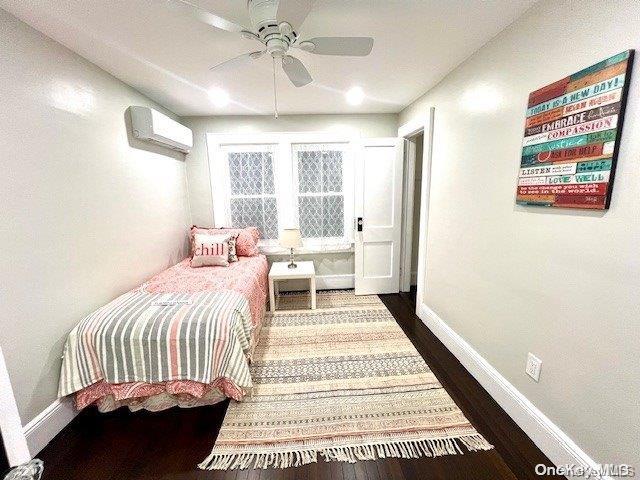 bedroom featuring dark wood finished floors, a wall unit AC, a ceiling fan, and baseboards