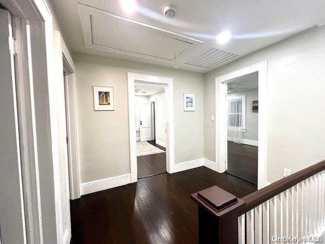 corridor with dark wood finished floors, attic access, and baseboards