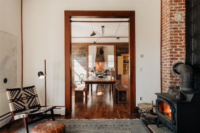 interior space with a baseboard heating unit, wood finished floors, and a wood stove