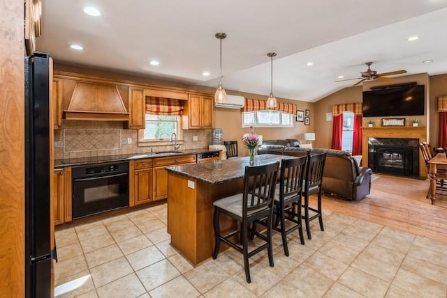 kitchen featuring open floor plan, a kitchen bar, black appliances, wall chimney exhaust hood, and a sink