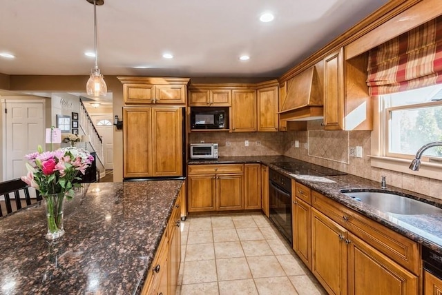 kitchen with brown cabinetry, black appliances, custom range hood, and a sink