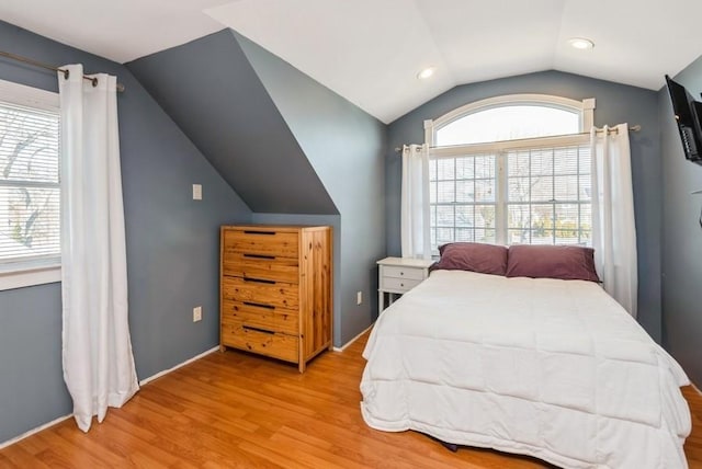 bedroom with vaulted ceiling, light wood-style flooring, and multiple windows