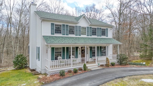 view of front facade with aphalt driveway, covered porch, roof with shingles, and a chimney