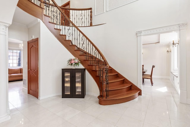 stairs featuring ornamental molding, a high ceiling, baseboards, and decorative columns