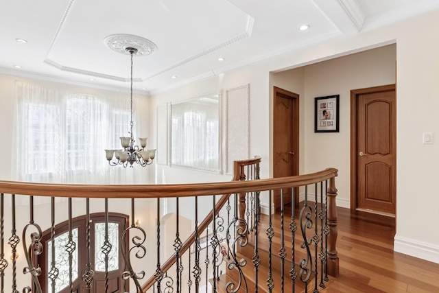 corridor with crown molding, a chandelier, a tray ceiling, wood finished floors, and plenty of natural light