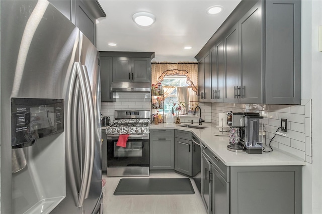 kitchen with a sink, gray cabinetry, light countertops, stainless steel appliances, and under cabinet range hood