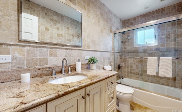 bathroom with tasteful backsplash, toilet, vanity, shower / bath combination with glass door, and tile walls