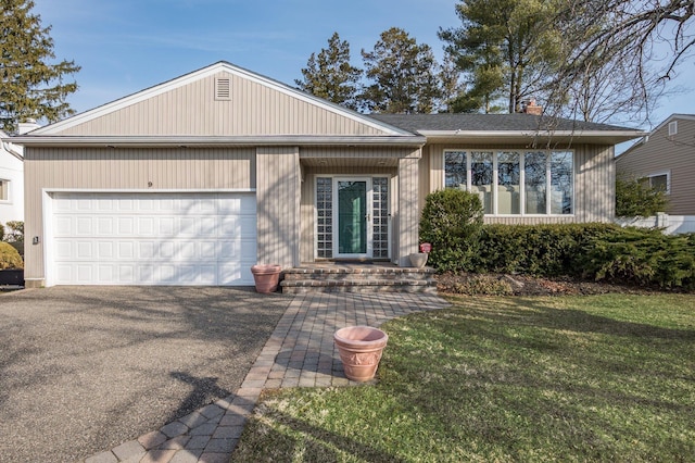 ranch-style house featuring a front yard, an attached garage, a chimney, and aphalt driveway