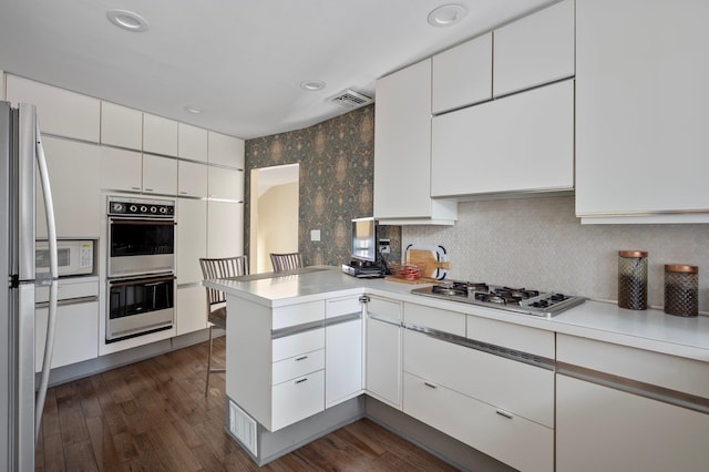 kitchen with white cabinets, appliances with stainless steel finishes, light countertops, and a peninsula